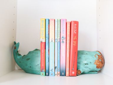 A wooden whale bookend holding several Roald Dahl books on a white shelf