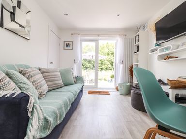 A living room with a sofa covered with a blanket and cushions a green chair and a wall-mounted TV at Penpoll Little Petherick Creek near Padstow