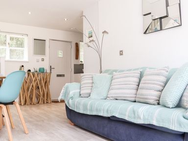 A living room with a sofa covered with blankets and cushions next to a wooden table and a floor lamp at Penpoll Little Petherick Creek near Padstow