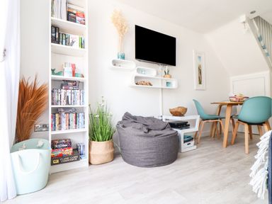 A living room with a bean bag chair a wall mounted TV a bookshelf and a dining table with blue chairs at Penpoll Little Petherick Creek near Padstow