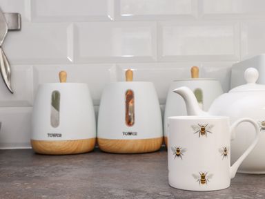 A kitchen countertop with white ceramic canisters with wooden knobs and a white teapot and mug with bee designs at Penpoll in Little Petherick Creek near Padstow