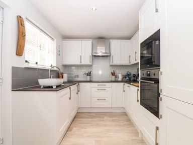 A white kitchen with cabinets a sink an oven and a microwave at Penpoll Little Petherick Creek near Padstow