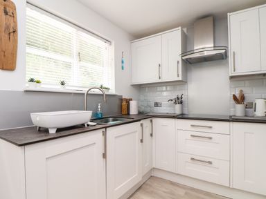 A kitchen with white cabinets a sink on the counter utensils and jars on the countertop at Penpoll Little Petherick Creek near Padstow
