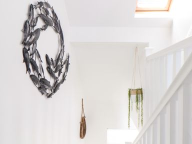 A white stairway with a metal fish wall art and a hanging plant at Penpoll Little Petherick Creek near Padstow