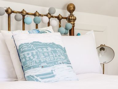 A bed with white pillows and a decorative cushion showing buildings and boats at Penpoll in Little Petherick Creek near Padstow