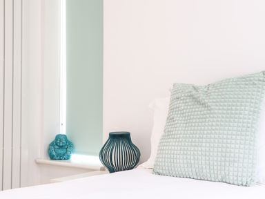 A bed with a textured pillow and a window sill with a blue Buddha statue and decorative object at Penpoll in Little Petherick Creek near Padstow