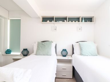A bedroom with two single beds with pillows a nightstand with a lamp and shelves with decorations above the beds at Penpoll in Little Petherick Creek near Padstow