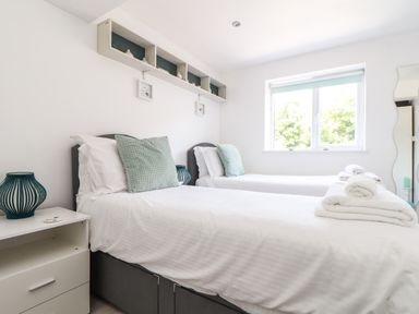 A bedroom with two single beds a nightstand with a lamp and a window at Penpoll Little Petherick Creek near Padstow
