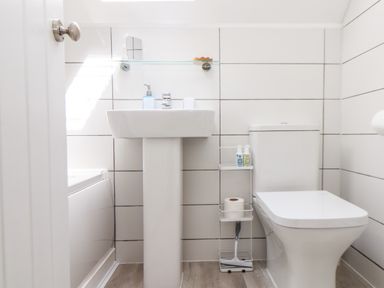 A bathroom with a pedestal sink a toilet a bathtub and a toilet paper holder with cleaning supplies at Penpoll Little Petherick Creek near Padstow