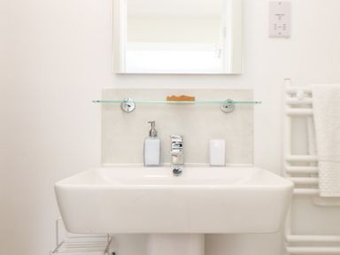 A bathroom sink with a soap dispenser toothbrush holder and towel near a mirror at Penpoll Little Petherick Creek near Padstow