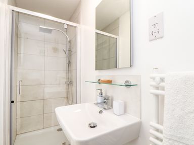 A bathroom with a shower enclosure and a wash basin with a glass shelf and mirror above it at Penpoll in Little Petherick Creek near Padstow
