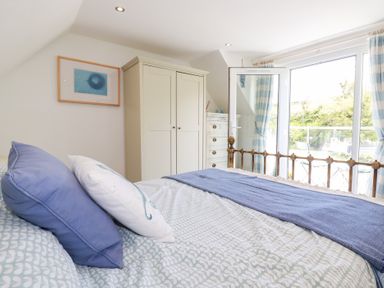 A bedroom with a bed with blue and white pillows a wardrobe a chest of drawers and glass doors with curtains at Penpoll Little Petherick Creek near Padstow