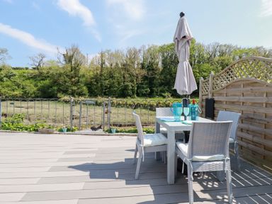 An outdoor patio with a dining table four chairs a closed umbrella and a wooden fence at Penpoll Little Petherick Creek near Padstow
