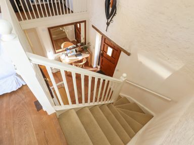 A staircase with beige carpet leading down to a hallway with a wooden door and a wooden table with chairs at The Old Barn in Colyton