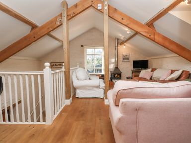An attic living area with wooden beams a white armchair a pink sofa a brown sofa a wood stove and a small television at The Old Barn in Colyton