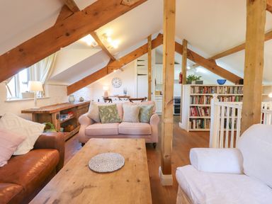 A living room with sofas a wooden coffee table exposed wooden beams and a bookshelf at The Old Barn in Colyton
