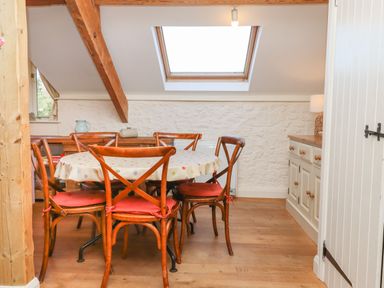 A dining area with a round table and wooden chairs under a skylight window at The Old Barn in Colyton