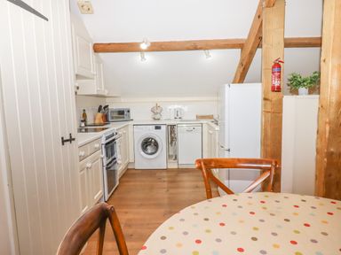 A kitchen with white cabinets washing machine dishwasher and refrigerator a wooden table with chairs and wooden beams at The Old Barn in Colyton