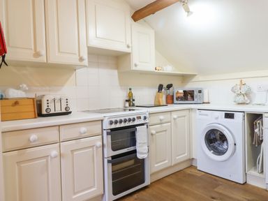A kitchen with white cabinets a stove washing machine toaster and microwave at The Old Barn in Colyton