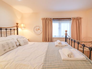 A bedroom with a metal bed frame white bedding pillows folded towels a lamp and checked curtains at The Old Barn in Colyton
