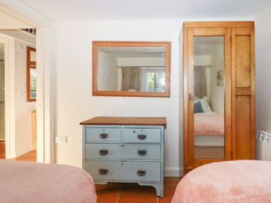 A bedroom with two beds covered in pink blankets a blue dresser with a wooden top a wooden wardrobe with a mirrored door and a wall mirror at The Old Barn in Colyton