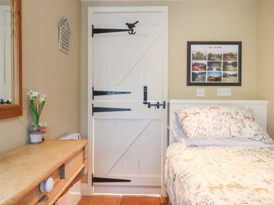 A bedroom with a wooden dresser a white divided door a bed with patterned bedding and a framed photo collage on the wall at The Old Barn in Colyton