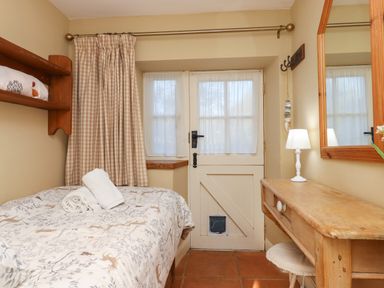 A bedroom with a bed beside a door with a pet flap and a wooden desk with a lamp and mirror at The Old Barn in Colyton
