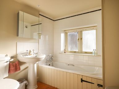A bathroom with a toilet sink mirror and bathtub under a window at The Old Barn in Colyton