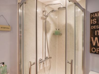 A corner shower enclosure with glass doors and chrome shower fixtures in a bathroom at The Old Barn in Colyton