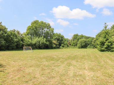 An open grass field with a small soccer goal and trees in the background at The Old Barn in Colyton