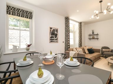 A dining table set with plates and pears in a living room with a sofa and armchair at Alice House Stone Cross Mansion in Ulverston