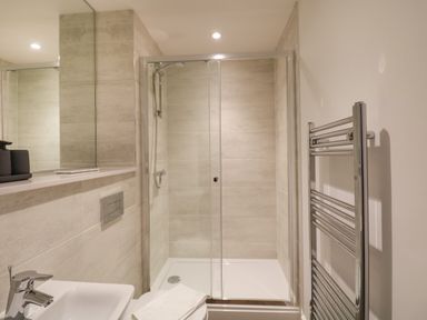A bathroom with a glass shower enclosure a sink a chrome towel rack and beige tiled walls at Alice House Stone Cross Mansion in Ulverston