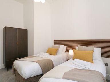 A bedroom with two single beds with pillows and blankets and a dark wardrobe at Alice House Stone Cross Mansion in Ulverston