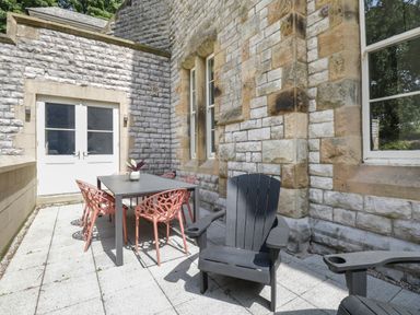 An outdoor patio with a black table and pink chairs next to a stone building at Alice House Stone Cross Mansion in Ulverston