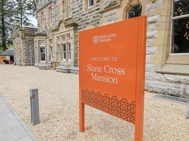 An orange welcome sign for Stone Cross Mansion outside a stone building at Alice House Stone Cross Mansion in Ulverston