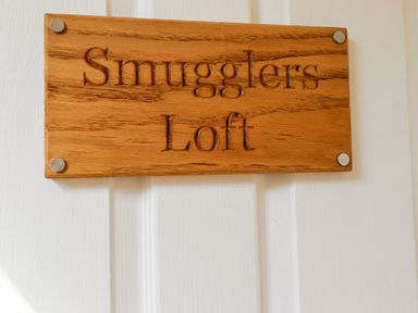 A wooden plaque with the words Smugglers Loft on a white door at Smugglers Loft in Looe