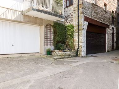 An outdoor area with two garage doors a small garden with green plants and stone walls at Smugglers Loft in Looe