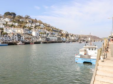 A river with boats docked and houses on a hillside in the background at Smugglers Loft in Looe