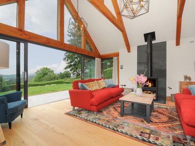 A living room with red sofas and a fireplace with a wood burner at Sandsgate Lodge Spinster's Rock near Chagford