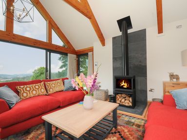 A living room with red sofas a wooden coffee table a fireplace and large windows showing a view at Sandsgate Lodge in Spinster's Rock near Chagford
