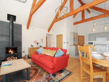 An open plan living room and kitchen with exposed wooden beams a red sofa and a wood burning stove at Sandsgate Lodge in Spinster's Rock near Chagford