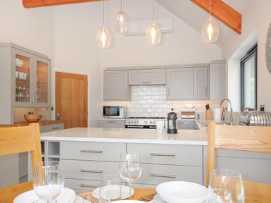 A kitchen with grey cabinets wooden chairs and pendant lights at Sandsgate Lodge Spinster's Rock near Chagford