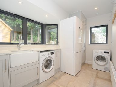 A laundry room with a washing machine dryer refrigerator and a sink with windows on two sides at Sandsgate Lodge Spinster's Rock near Chagford