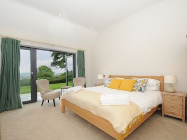 A bedroom with a wooden bed two bedside tables two chairs and glass doors opening to a garden at Sandsgate Lodge in Spinster's Rock near Chagford