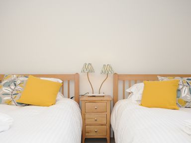 A bedroom with two single beds with yellow and patterned cushions and a wooden nightstand with two lamps at Sandsgate Lodge in Spinsters Rock near Chagford
