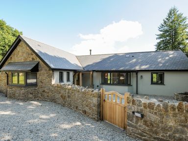 A stone and stucco house with a wooden gate and gravel driveway at Sandsgate Lodge in Spinster's Rock near Chagford