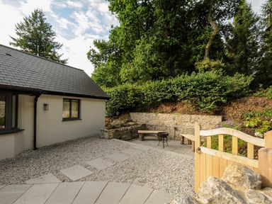 An outdoor patio area with stone pathway gravel and benches next to a house and greenery at Sandsgate Lodge Spinster's Rock near Chagford