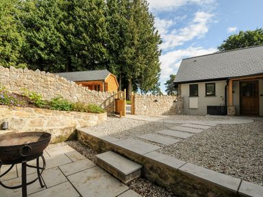 A stone patio with steps and a fire pit beside a gravel pathway and stone wall at Sandsgate Lodge Spinster's Rock near Chagford