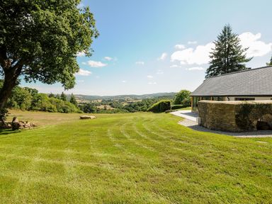 A grassy lawn with a stone wall and a house with a gray roof overlooking hills and trees at Sandsgate Lodge in Spinster's Rock near Chagford