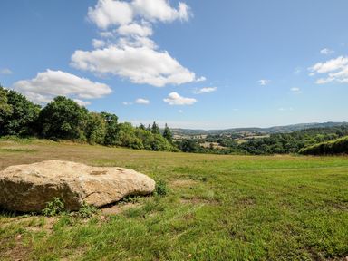 A large rock on grassy land with trees and hills under a blue sky at Sandsgate Lodge in Spinster's Rock near Chagford